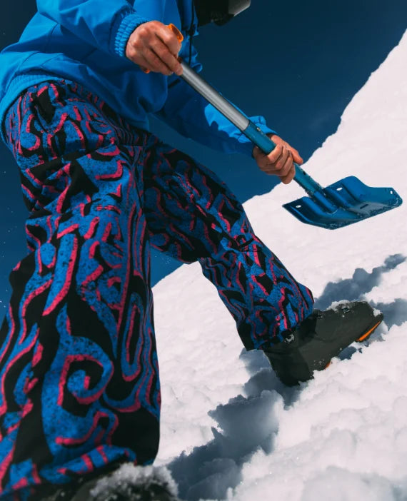 Person shoveling snow wearing a blue jacket and patterned pants.