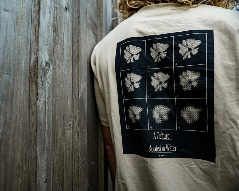 Person wearing a white t-shirt with a black graphic design on the back, standing against a wooden wall - urbaneight 